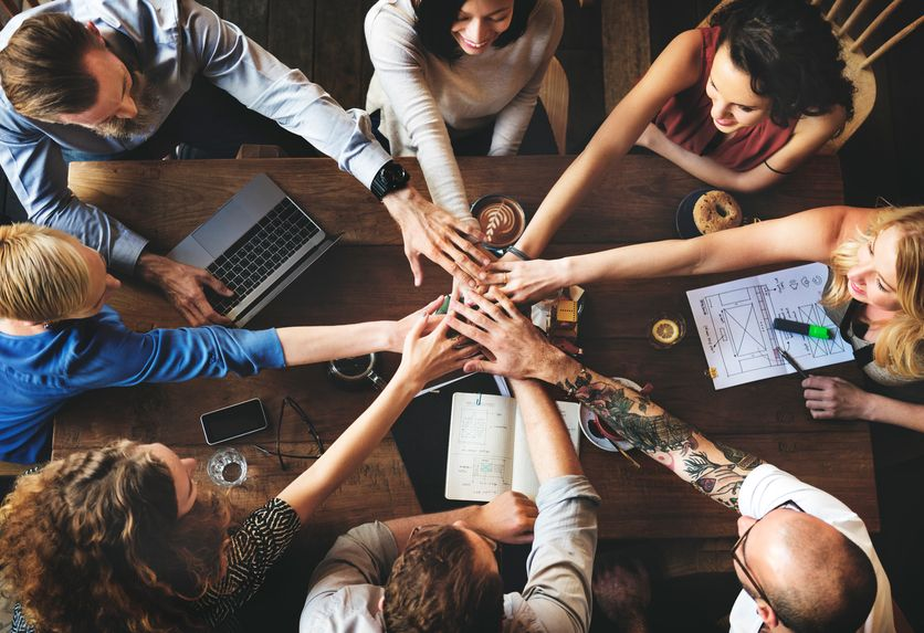 Team placing hands together over a workspace during business collaboration.
